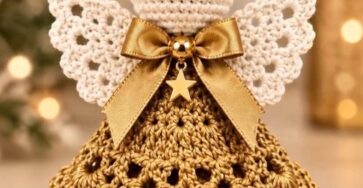 A detailed crochet angel ornament featuring a layered gold skirt, white wings, bead halo, and a gold bow with a star charm.