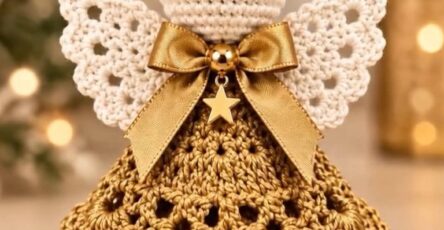 A detailed crochet angel ornament featuring a layered gold skirt, white wings, bead halo, and a gold bow with a star charm.