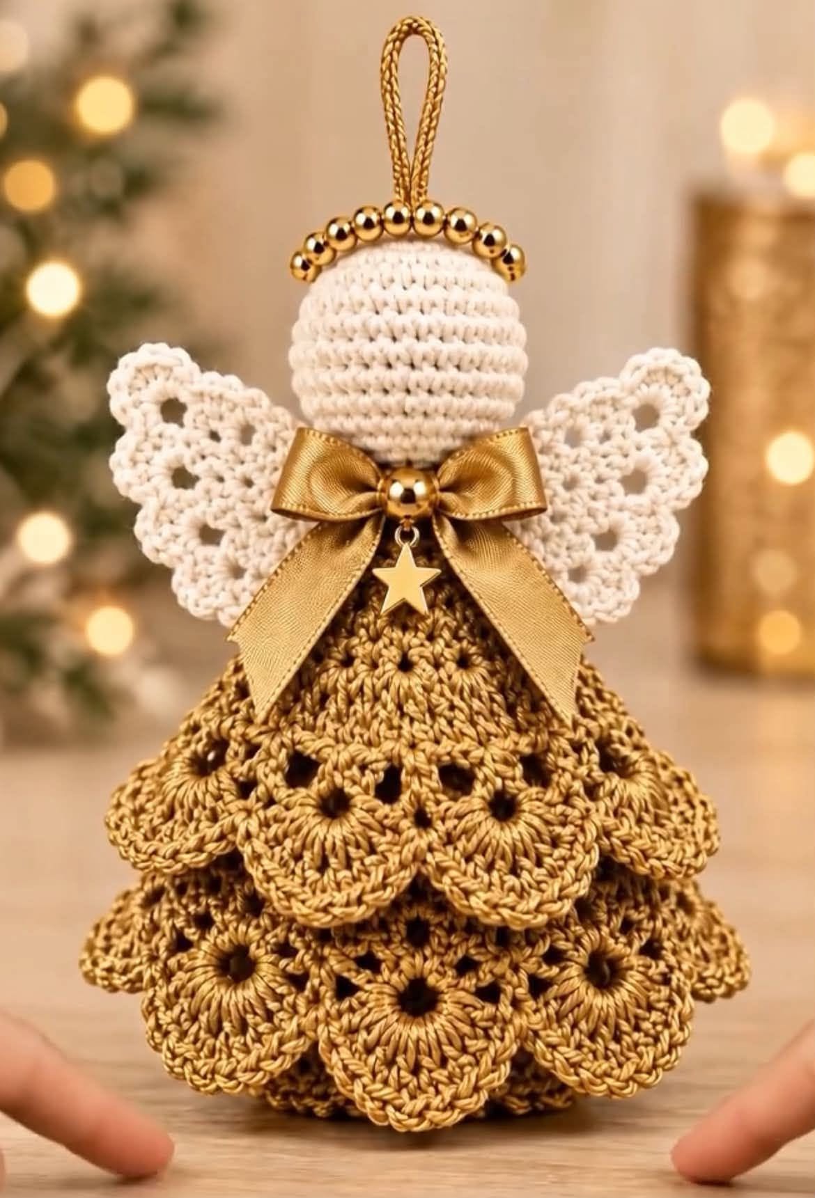 A detailed crochet angel ornament featuring a layered gold skirt, white wings, bead halo, and a gold bow with a star charm.