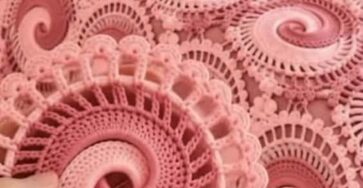 A pink crocheted blanket and pillow set featuring intricate swirling circular motifs, with a close-up of a single motif held in hand.