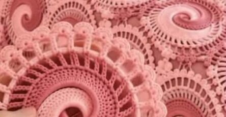 A pink crocheted blanket and pillow set featuring intricate swirling circular motifs, with a close-up of a single motif held in hand.