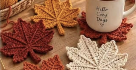 Crocheted maple leaf coasters in autumn colors arranged on a wooden table with a cozy mug.