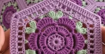 A crochet blanket and pillows made from hexagonal motifs with purple flower centers and light green leaves, joined together.
