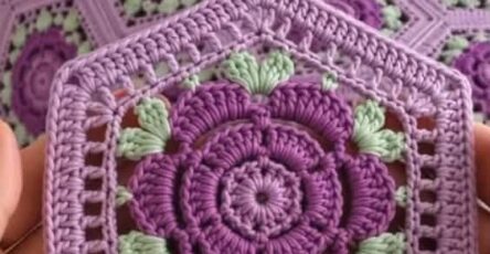 A crochet blanket and pillows made from hexagonal motifs with purple flower centers and light green leaves, joined together.