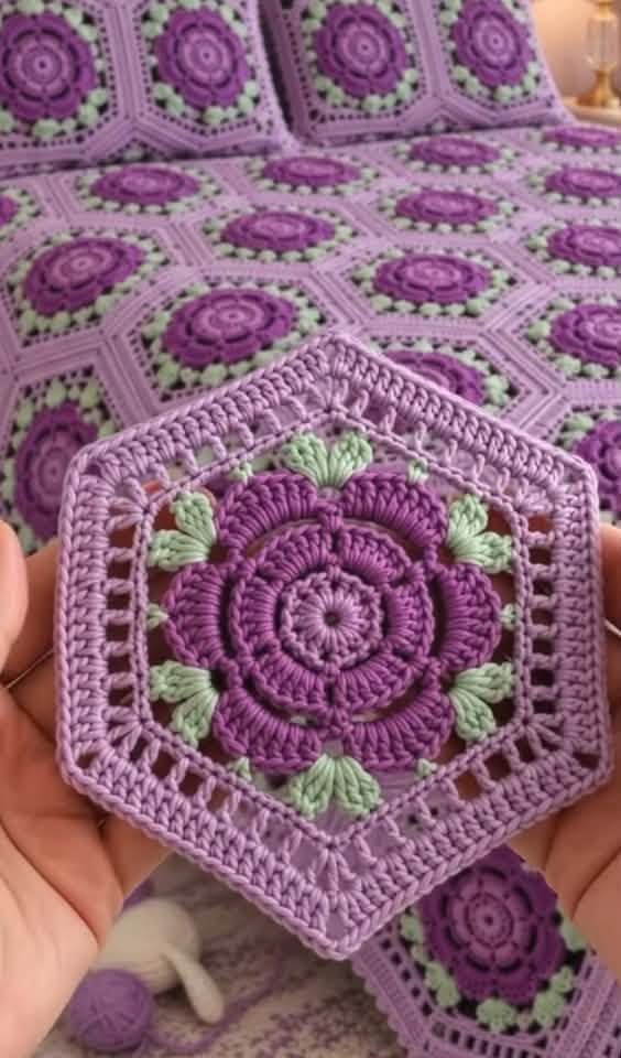 A crochet blanket and pillows made from hexagonal motifs with purple flower centers and light green leaves, joined together.