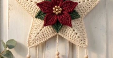 A festive crochet wall hanging with a cream star, red poinsettia, green leaves, hanging trees, heart, bells, and a red ribbon bow.