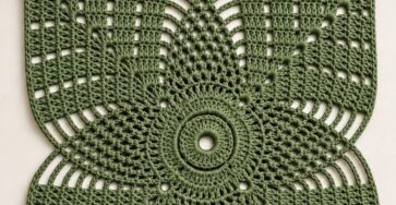A green crochet square with a geometric flower motif in the center, surrounded by open and solid stitch panels.