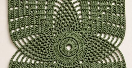 A green crochet square with a geometric flower motif in the center, surrounded by open and solid stitch panels.