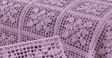 Lavender crochet bedspread made from floral granny squares with lacy grid borders, covering a bed in a softly decorated room.
