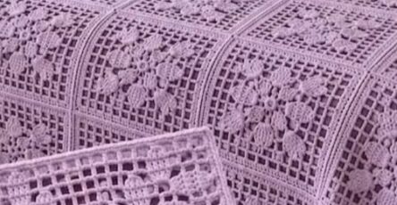 Lavender crochet bedspread made from floral granny squares with lacy grid borders, covering a bed in a softly decorated room.