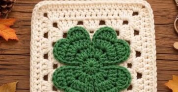 Crochet granny square with a green four-leaf clover in the center, bordered by white yarn.