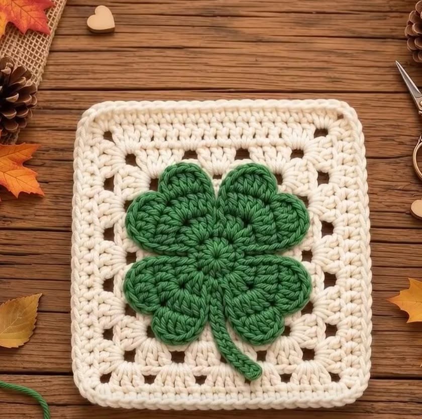 Crochet granny square with a green four-leaf clover in the center, bordered by white yarn.