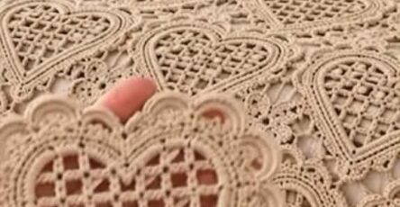 A close-up of a beige crochet bedspread made of lace heart motifs joined together, with a matching pillow.