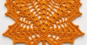 A crocheted doily shaped like a maple leaf in rich orange yarn, with openwork details and a central vein design.