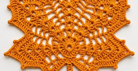 A crocheted doily shaped like a maple leaf in rich orange yarn, with openwork details and a central vein design.