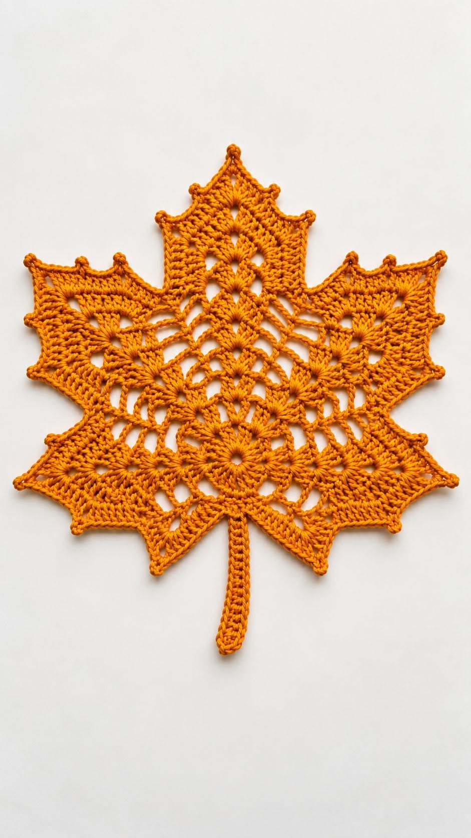 A crocheted doily shaped like a maple leaf in rich orange yarn, with openwork details and a central vein design.