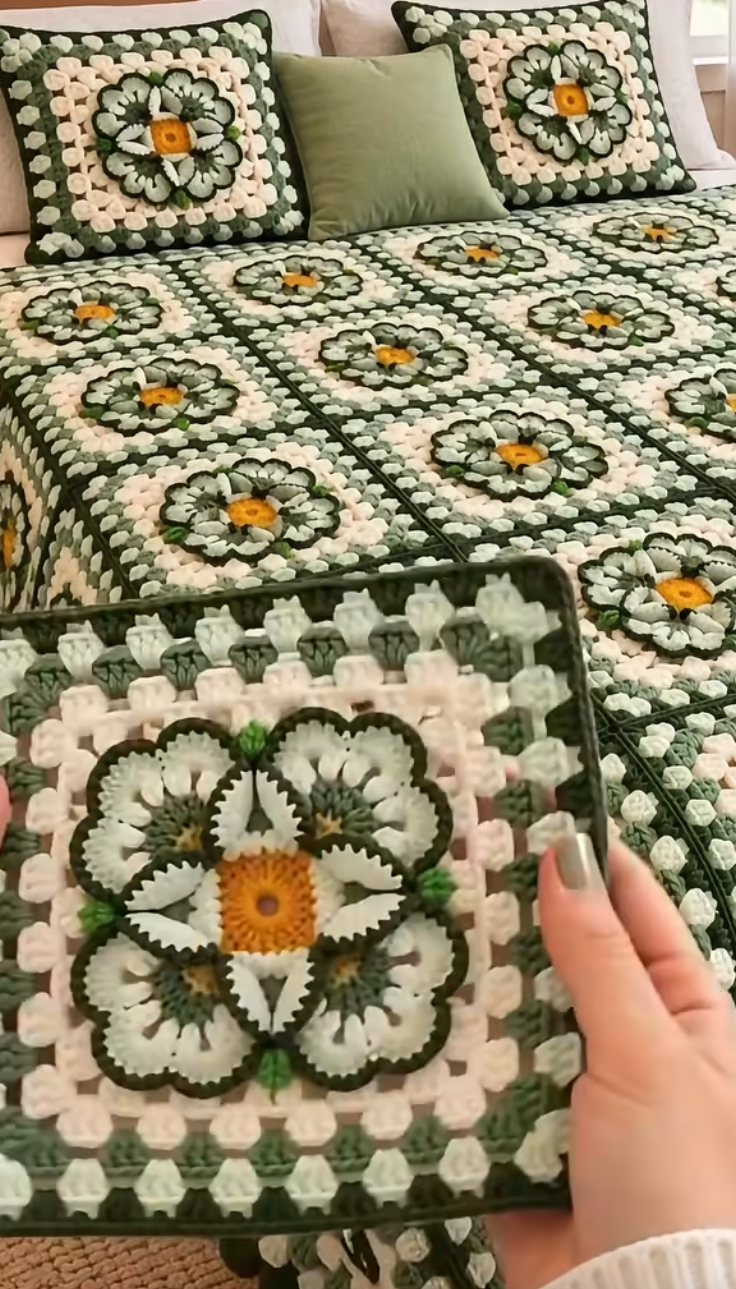 A crochet bedspread and pillows featuring large, multi-colored granny squares with a central flower motif in green, white, and yellow.