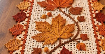Crochet table runner with large maple leaves in fall colors, acorn accents, and scalloped leaf border on a rectangular lacy background.