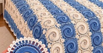 A bed covered with a handmade crochet bedspread made of blue and cream spiral motif squares joined together, with matching pillows and detailed edging.