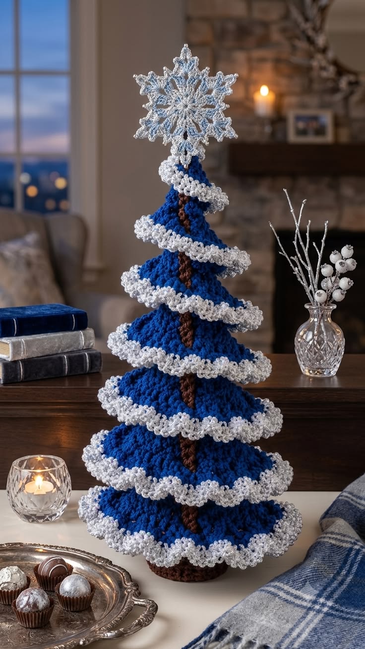 A crocheted Christmas tree with blue tiers, silver ruffled edges, brown trunk, and a silver-blue snowflake topper displayed as a holiday centerpiece.