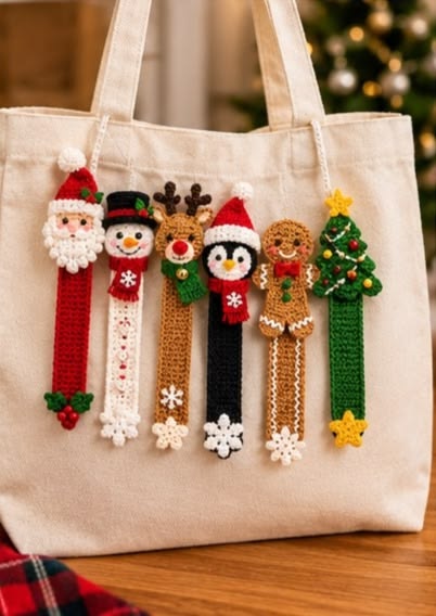 Six colorful crocheted Christmas character bookmarks, including Santa, snowman, reindeer, penguin, gingerbread, and a tree, displayed on a tote bag.