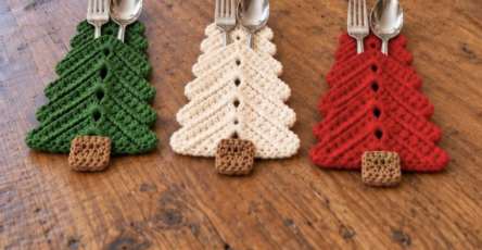 Three crochet Christmas tree utensil holders in green, white, and red with brown trunks, each holding a fork and spoon.