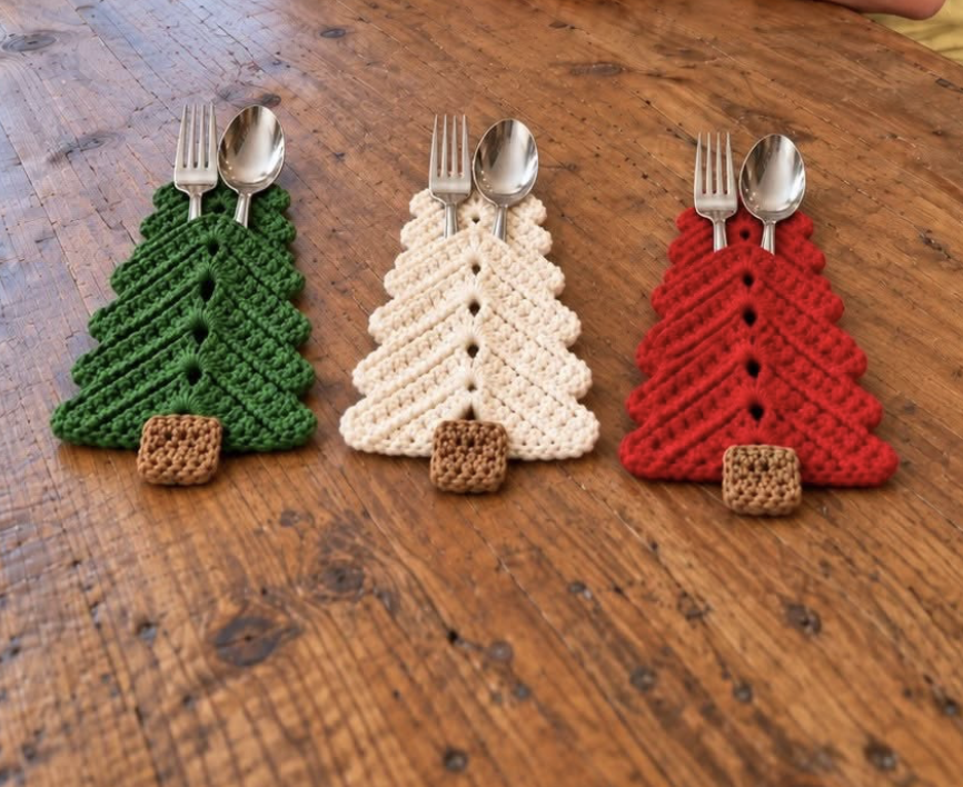 Three crochet Christmas tree utensil holders in green, white, and red with brown trunks, each holding a fork and spoon.