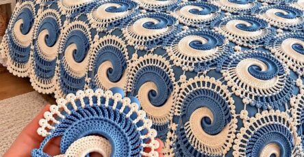 Blue and white crochet bedspread with intricate spiral motifs and coordinated pillows in a well-lit, cozy bedroom.