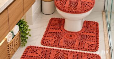 A four-piece crocheted bathroom set in burnt orange, including a rectangular rug, a contour rug, a toilet lid cover, and a tank topper with sunburst motifs.
