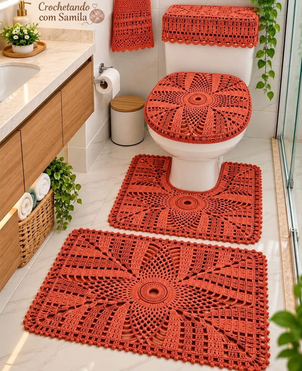 A four-piece crocheted bathroom set in burnt orange, including a rectangular rug, a contour rug, a toilet lid cover, and a tank topper with sunburst motifs.