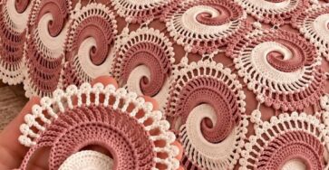 A hand holds a two-tone crochet swirl motif, shown alongside a bedspread made of many joined spiral motifs in dusty rose and ivory.
