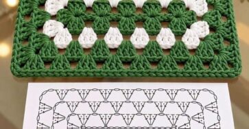 A green and white rectangular crochet mat with a classic granny stitch design, placed on a glass table beside a crochet chart diagram.