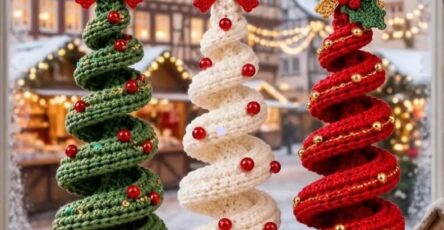 Three spiral crochet Christmas tree ornaments in green, white, and red, decorated with beads, bows, and bells, hanging in a cozy holiday setting.