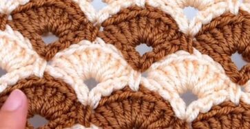 A close-up of a two-color crochet project featuring overlapping fan shell motifs in caramel and cream with openwork arches.