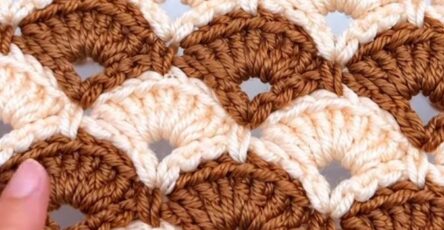 A close-up of a two-color crochet project featuring overlapping fan shell motifs in caramel and cream with openwork arches.