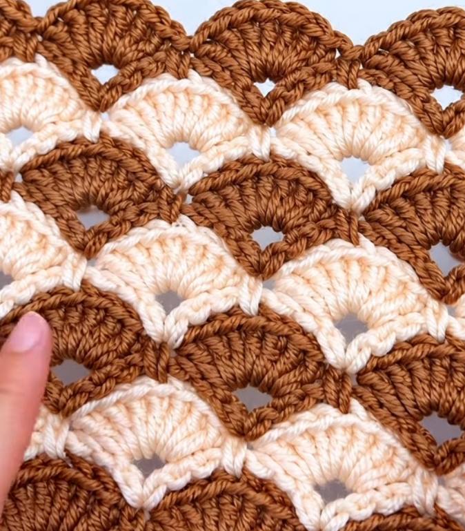 A close-up of a two-color crochet project featuring overlapping fan shell motifs in caramel and cream with openwork arches.