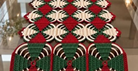 A festive crochet table runner in red, green, and cream, with alternating diamond motifs and circular fan sections, arranged in a long geometric pattern.