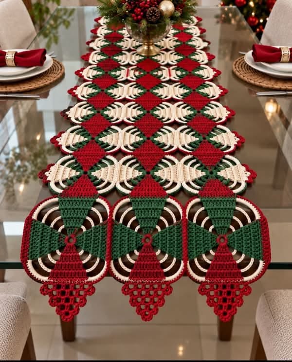 A festive crochet table runner in red, green, and cream, with alternating diamond motifs and circular fan sections, arranged in a long geometric pattern.