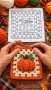 A crochet granny square featuring an orange pumpkin with green leaves in the center, bordered by white and orange rounds.