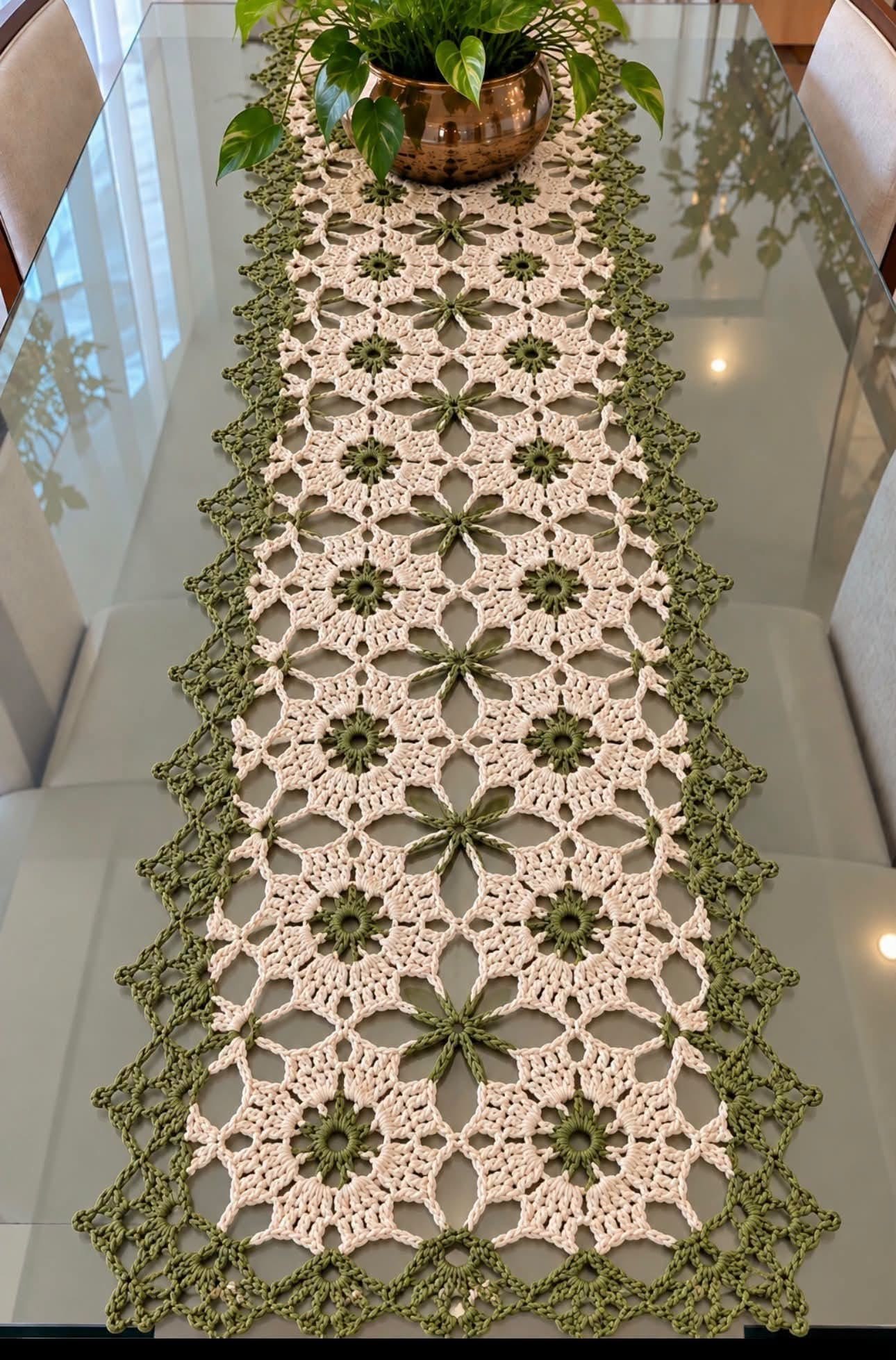 A crochet table runner with green and cream floral motifs arranged in lacy geometric patterns and bordered with a delicate green edge.