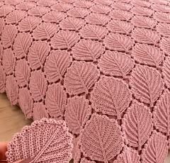 A bedspread and pillows made of joined crochet leaf motifs in dusty pink yarn, displayed on a large bed.