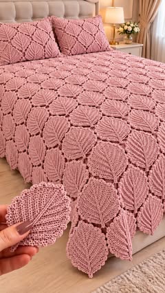 A bedspread and pillows made of joined crochet leaf motifs in dusty pink yarn, displayed on a large bed.