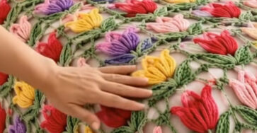 A crochet bedspread and pillow covers featuring colorful 3D tulip motifs joined with green leafy yarn, forming a lacy floral pattern.