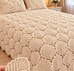 A cream-colored crocheted bedspread with repeating leaf motifs, displayed on a neatly made bed with matching pillows.