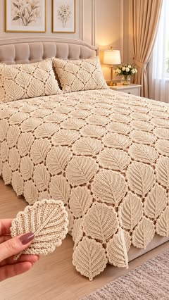 A cream-colored crocheted bedspread with repeating leaf motifs, displayed on a neatly made bed with matching pillows.