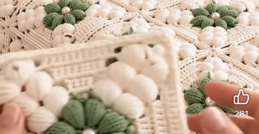 A crochet bedspread made from green and white granny squares featuring textured flower motifs.