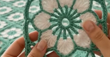 Lacy crochet granny square motif with a white flower center and green openwork border, used in a bedspread and pillow.
