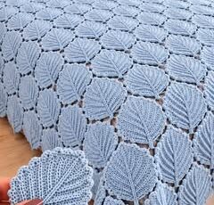 Light blue crochet bedspread with closely joined leaf motifs, displayed on a bed with matching pillow shams.