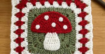 Crochet granny square with a red mushroom motif, white spots, green background, and alternating red and white granny borders.
