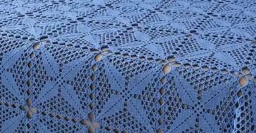 A blue crochet bedspread and matching pillow covers made with intricate lace square motifs, displayed on a neatly made bed.